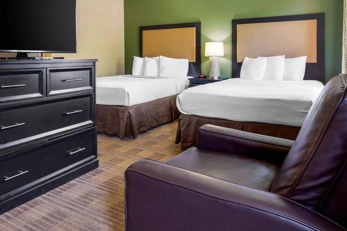 A hotel room with two beds, a TV, a desk, and a chair.