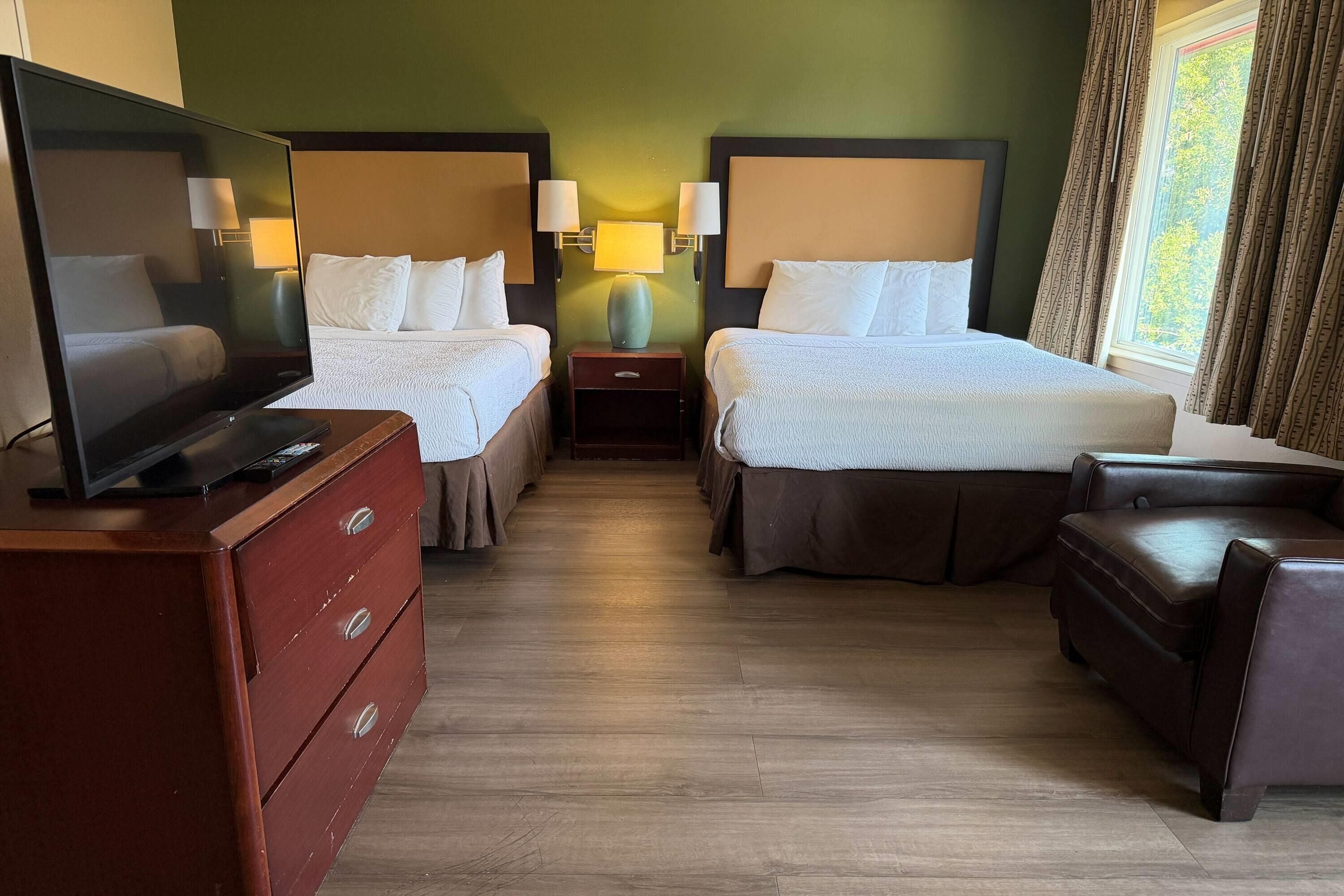 A hotel room with two beds, a TV, a dresser, and a window with curtains.