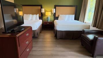 A hotel room with two beds, a TV, a dresser, and a window with curtains.