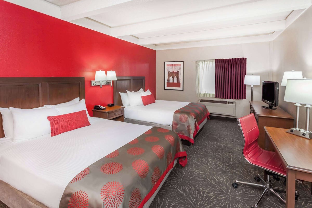 A hotel room with two beds, a desk, a chair, a TV, and a window with curtains.