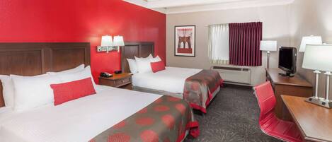 A hotel room with two beds, a desk, a chair, a TV, and a window with curtains.