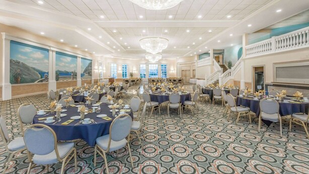 A large banquet hall with round tables, chairs, and a chandelier. - Ramada Hotel & Conference Center by Wyndham Hammond (Hammond)