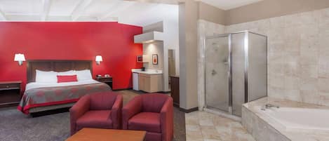 A hotel room with a bed, two armchairs, a wooden table, a bathroom with a bathtub, and a shower.