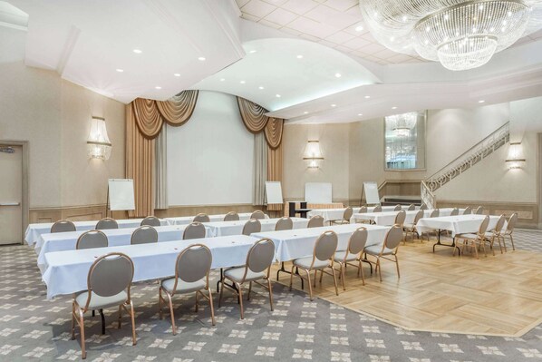 A conference room with multiple tables and chairs, a chandelier, and a staircase.