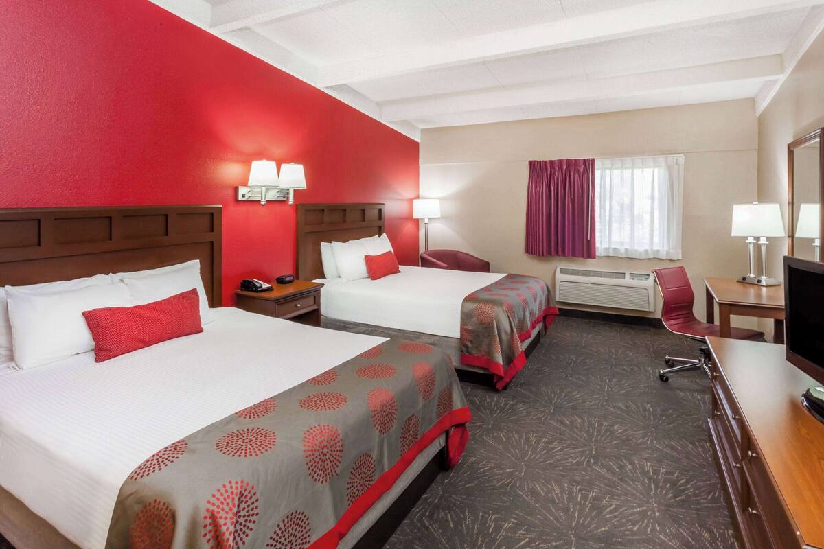 A hotel room with two beds, a desk, a chair, a TV, and a window with curtains.