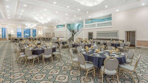 A banquet hall with round tables, chairs, chandeliers, and a patterned carpet. - Ramada Hotel & Conference Center by Wyndham Hammond (Hammond)
