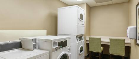 A laundry room with stacked washers and dryers, a small table with chairs, and a wall-mounted TV.