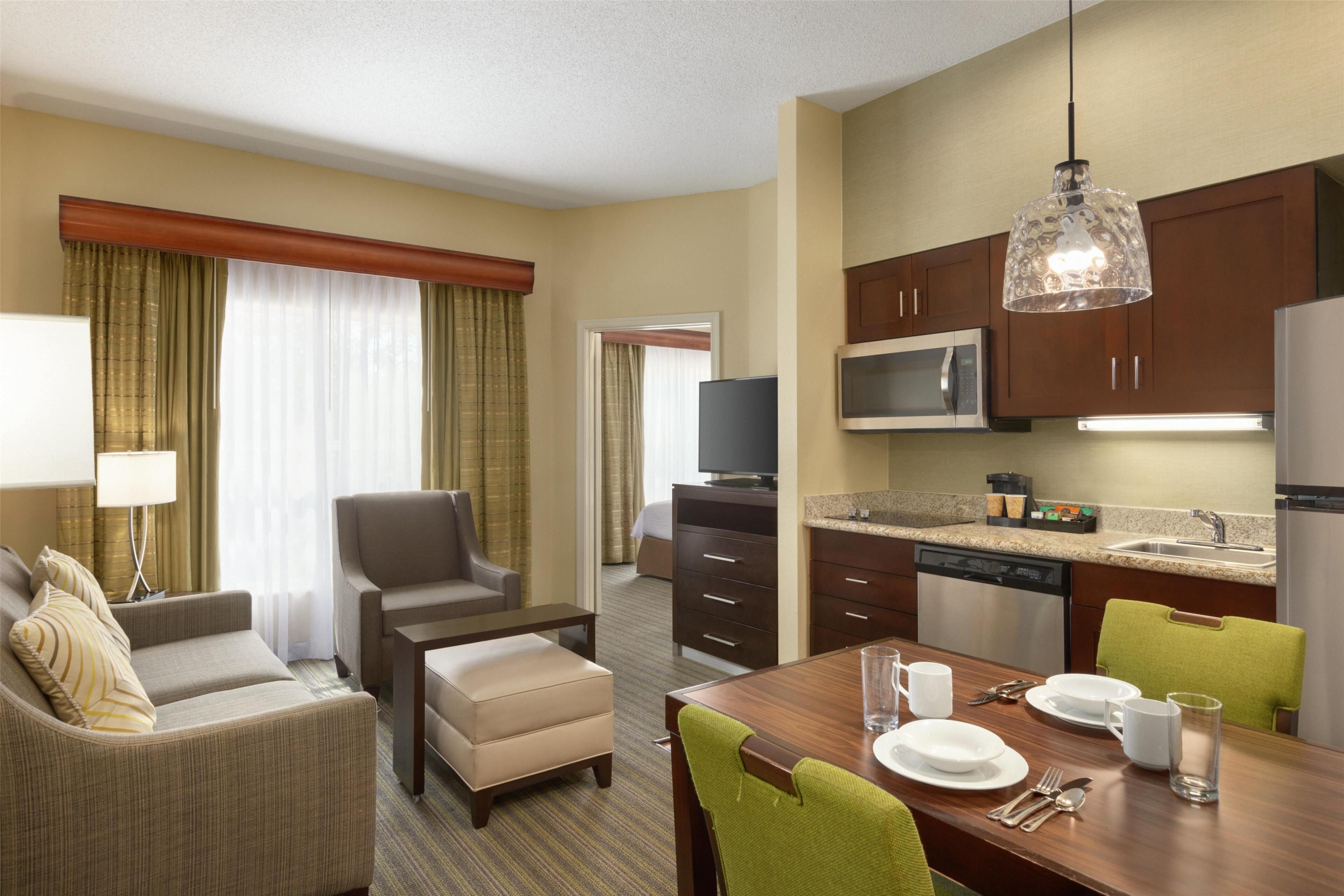 A hotel room with a living area, dining table, kitchenette, and a television.