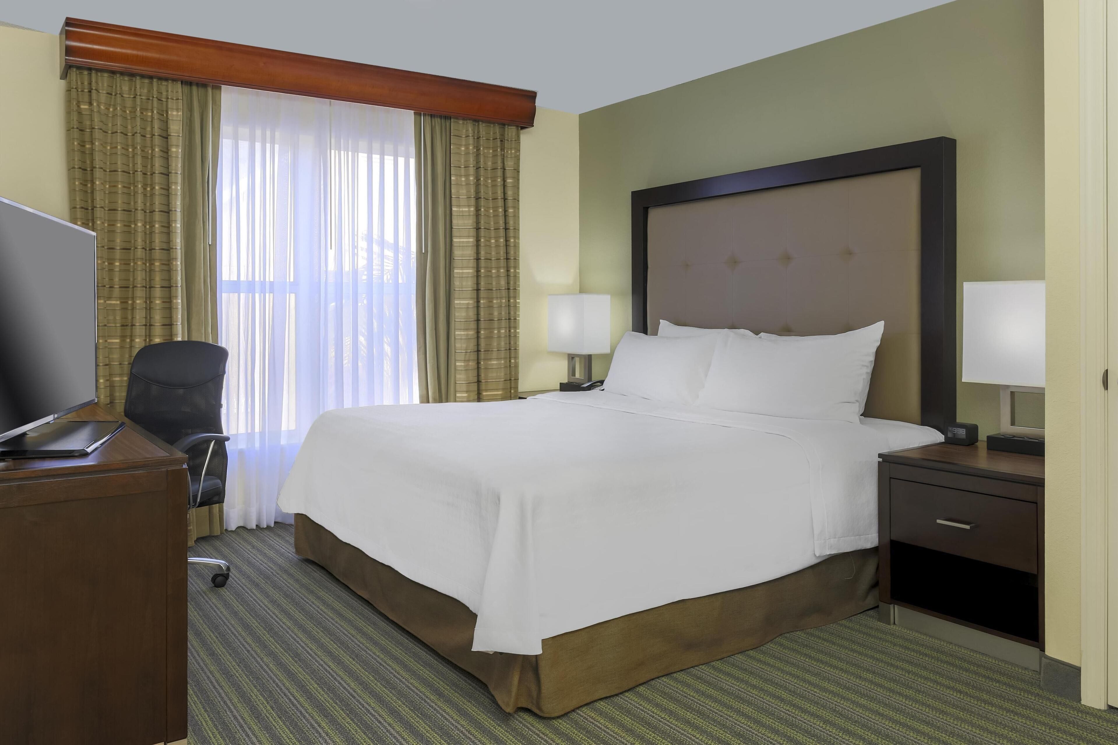 A hotel room with a large bed, a desk with a computer, a chair, and a TV.