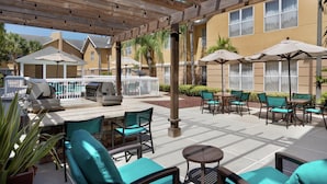 An outdoor patio area with wooden pergola, outdoor seating, and a pool in the background.