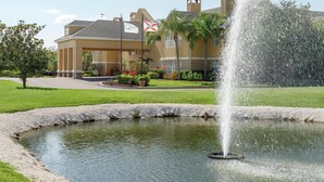 A hotel with a fountain in the courtyard, a flag, and a well-maintained lawn.