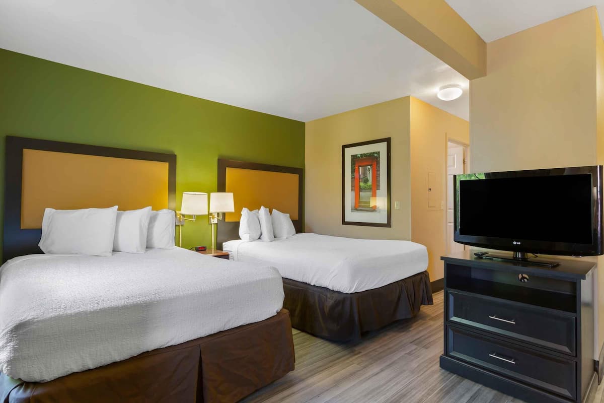 A hotel room with two beds, a flat-screen TV, a desk with a lamp, and a framed picture on the wall.