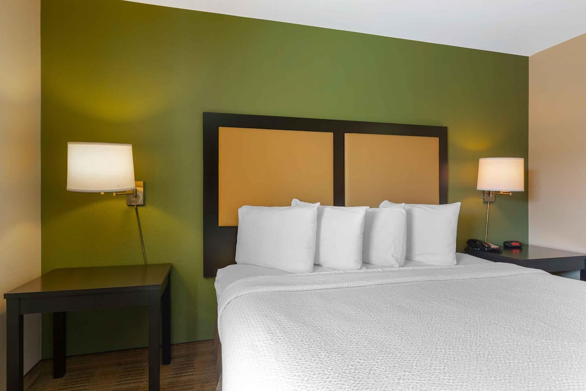 A hotel room with a large bed, two bedside tables, and two wall-mounted lamps.