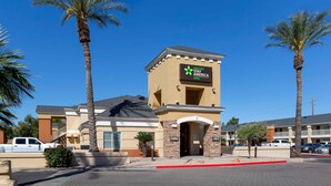 Un hôtel de la chaîne Stay America, reconnaissable à son panneau indiquant la présence de suites spacieuses, à son entrée et à son parking agrémenté de palmiers.