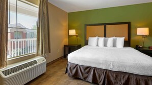 Une chambre d’hôtel avec un grand lit, deux lampes de chevet, une fenêtre avec des rideaux et un appareil de climatisation.