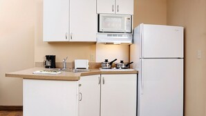 A compact kitchen with white cabinets, a microwave, a refrigerator, a sink, and a toaster.