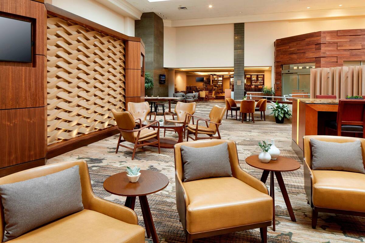 A hotel lobby with leather armchairs, a bar area, and a seating area with a patterned carpet.