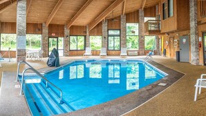 An indoor swimming pool with clear views of the outdoors, wooden beams, and a covered seating area. - Baymont by Wyndham Delaware (Delaware)