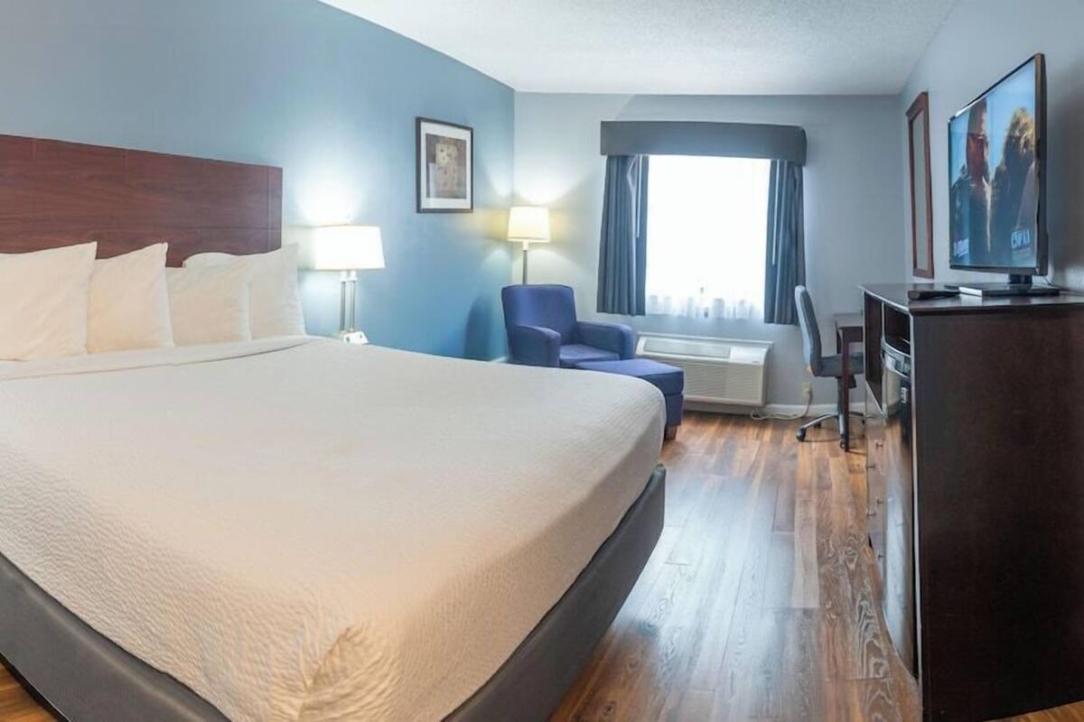 A hotel room with a large bed, a desk, a chair, a television, and a window with curtains.