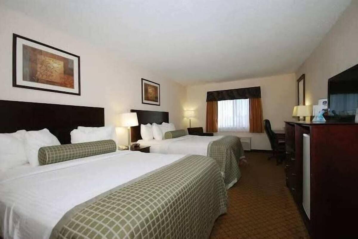 A hotel room with two beds, a desk, a chair, and a television.