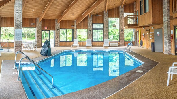 A large indoor swimming pool with wooden beams and brick walls, surrounded by lounge chairs and a covered seating area. - Baymont by Wyndham Delaware (Delaware)