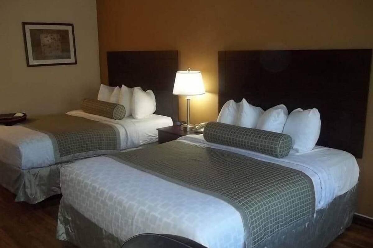 A hotel room with two beds, each with a headboard, a bedside table with a lamp, and a framed picture on the wall.
