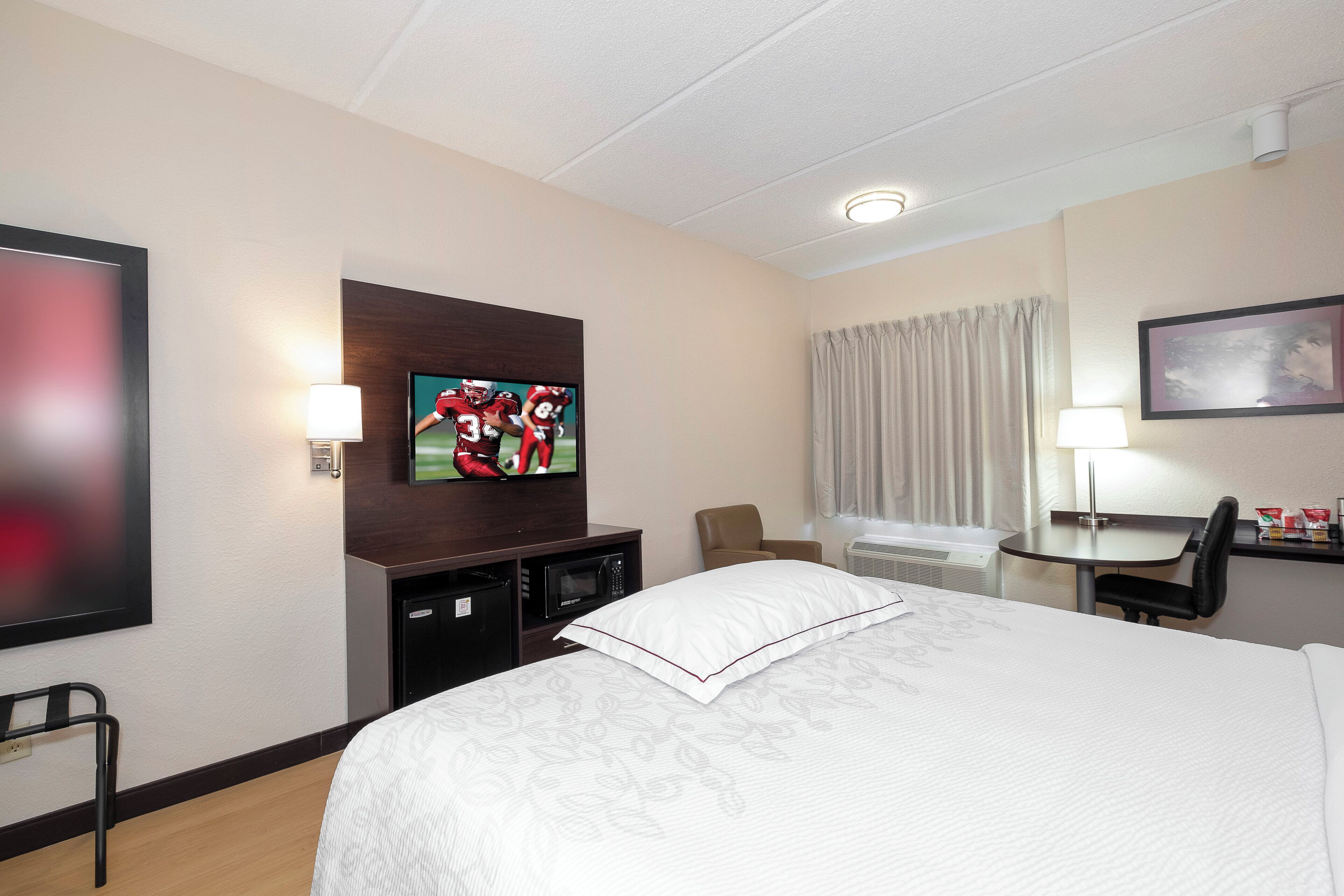 A hotel room with a bed, a television, a desk, a chair, and a window with curtains.