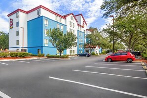 Un hôtel à plusieurs étages, avec une façade bleue et blanche, un toit rouge et un parking rempli de voitures.