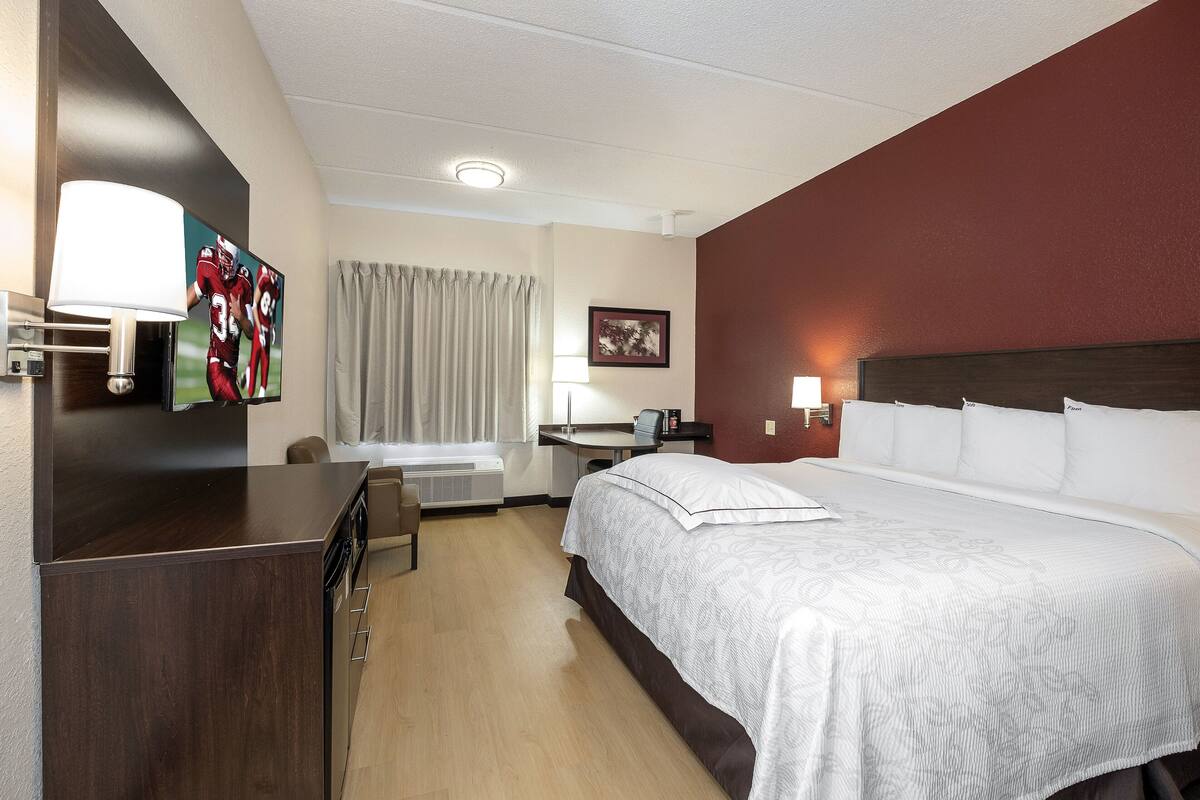 Ein Hotelzimmer mit einem Bett, einem Schreibtisch, einem Sessel, einem Fernseher und einer Lampe.