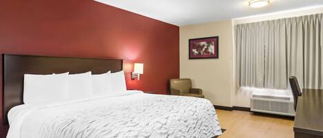 Habitación de hotel con una cama grande, un escritorio, una silla, una lámpara de pared y un ventanal con cortinas.