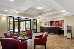 Un hall d’hôtel avec des fauteuils rouges, un comptoir d’accueil et un kiosque numérique.