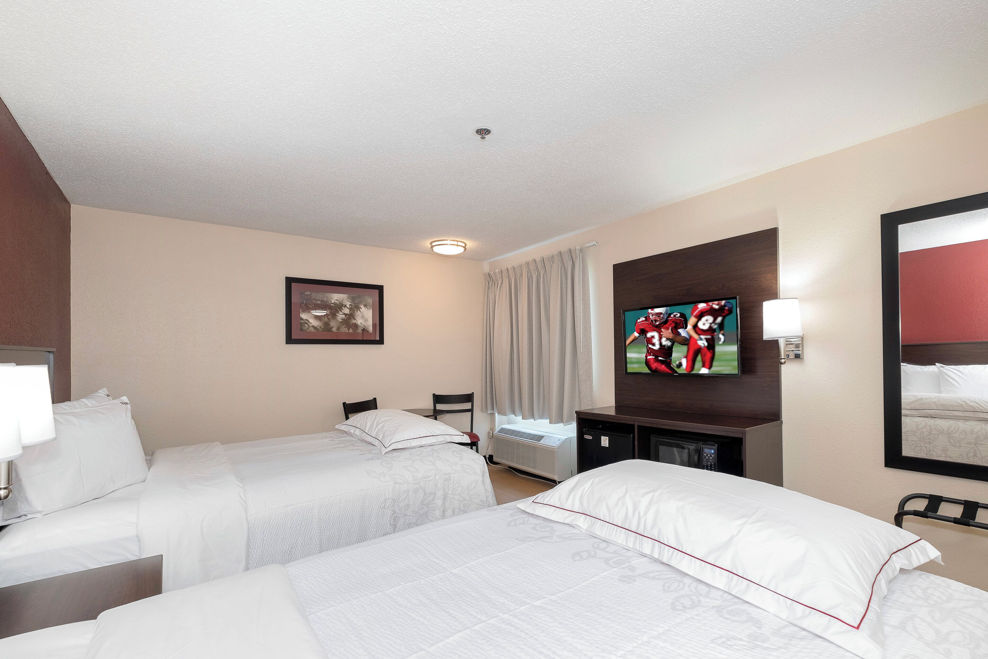 A hotel room with two beds, a television, a desk, and a window with curtains.