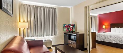 A hotel room with a sofa, a TV, a desk, a bed, and a window with curtains.