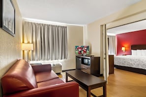 Habitación de hotel con sofá, televisión, escritorio, cama y ventana con cortinas.