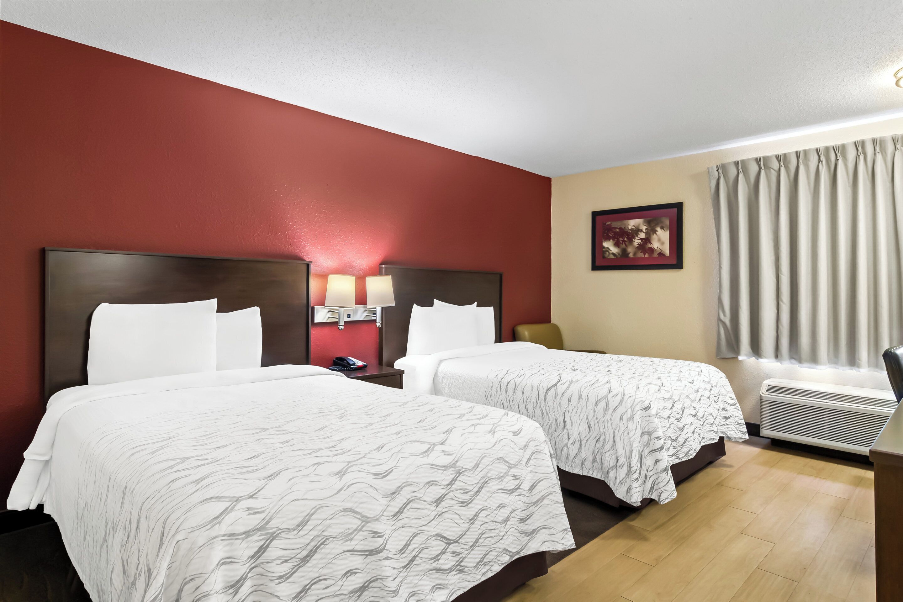 A hotel room with two beds, a desk, a chair, a telephone, and a picture on the wall.