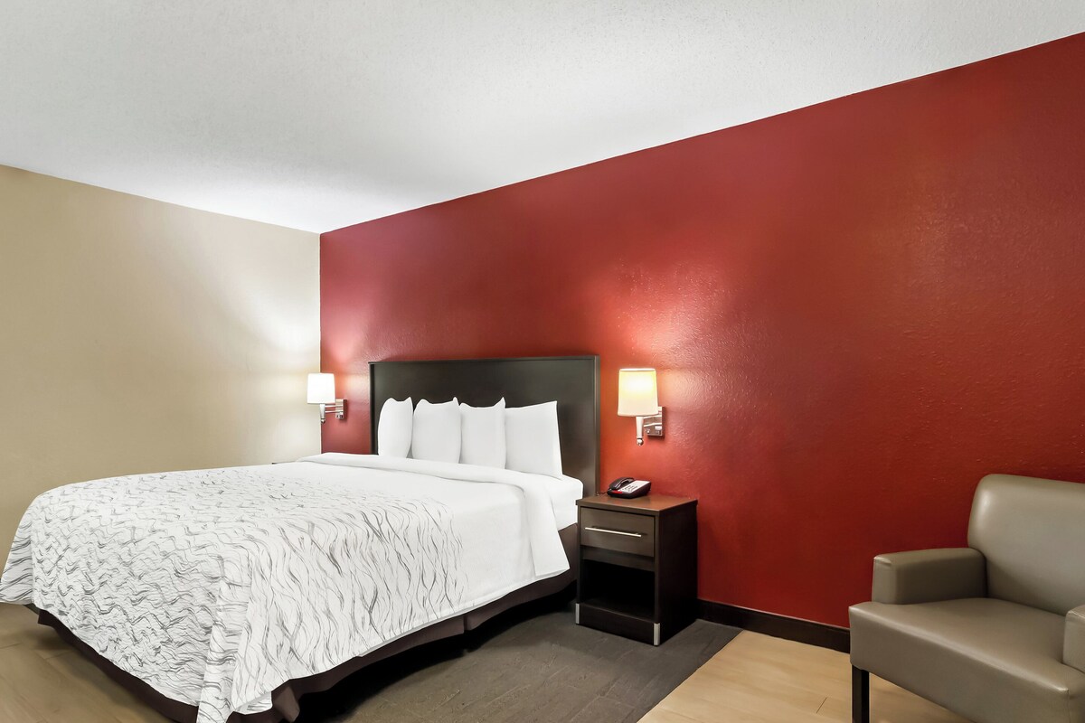 Une chambre d’hôtel avec un lit, des tables de chevet, une chaise et des murs rouges.