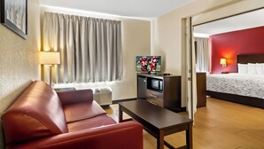 Une chambre d’hôtel équipée d’un canapé, d’une télévision, d’un bureau, d’un lit et d’une fenêtre avec des rideaux.