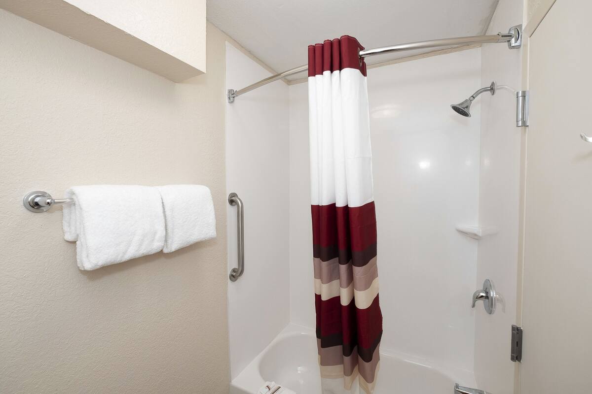 A shower with a white curtain and a handheld showerhead.