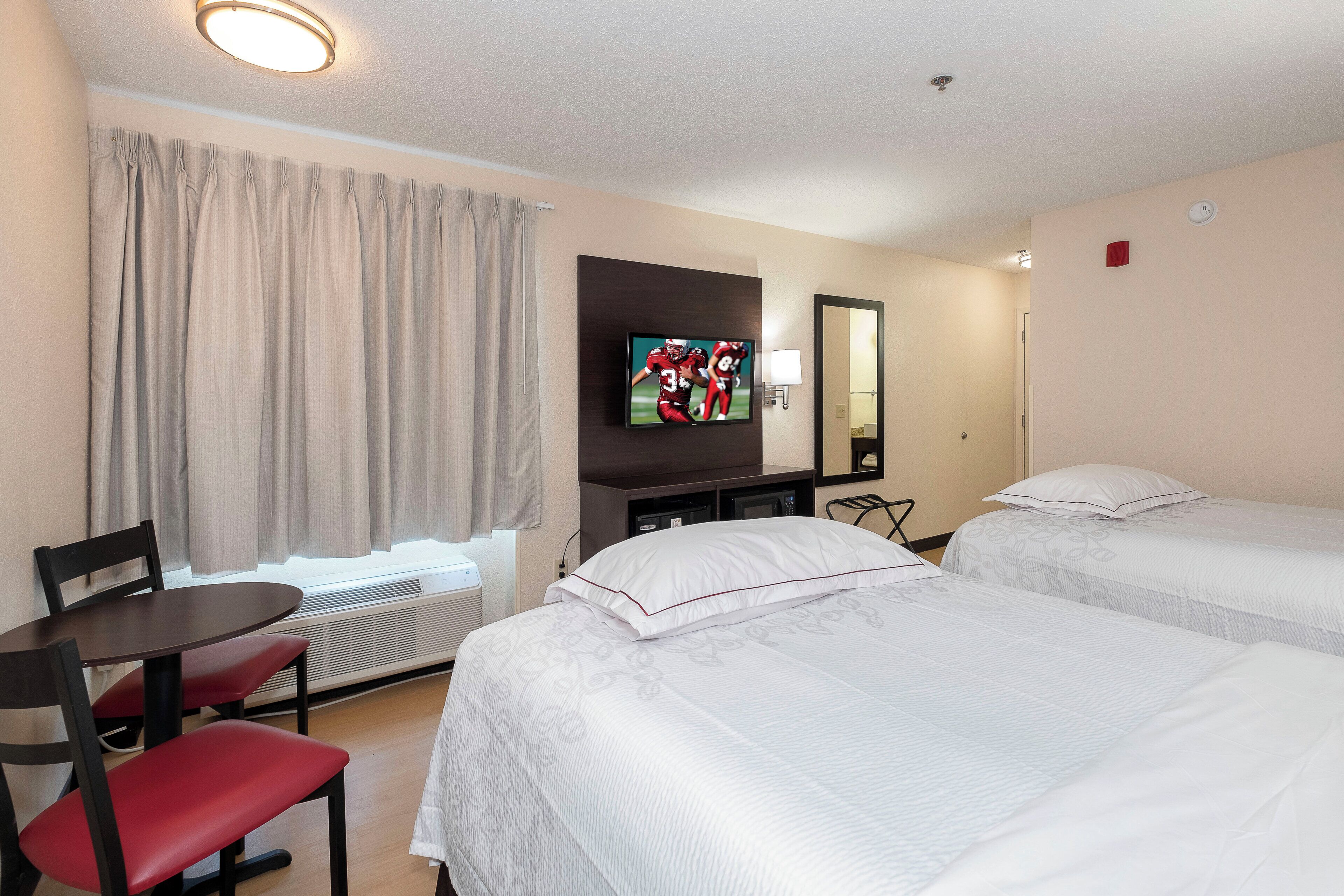 A hotel room with two beds, a TV, a desk, and a chair.