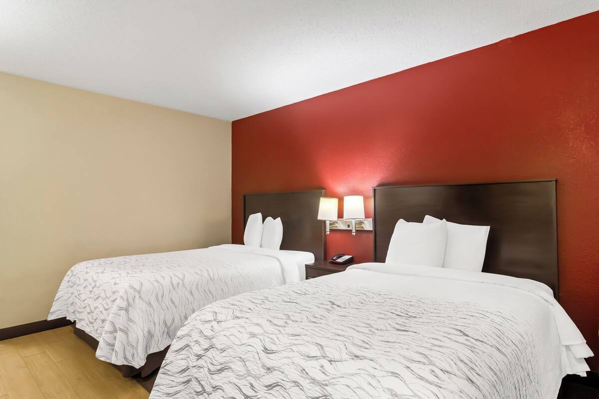 Ein Hotelzimmer mit zwei Betten, einer roten Akzentwand und einem Nachttisch mit Lampe.