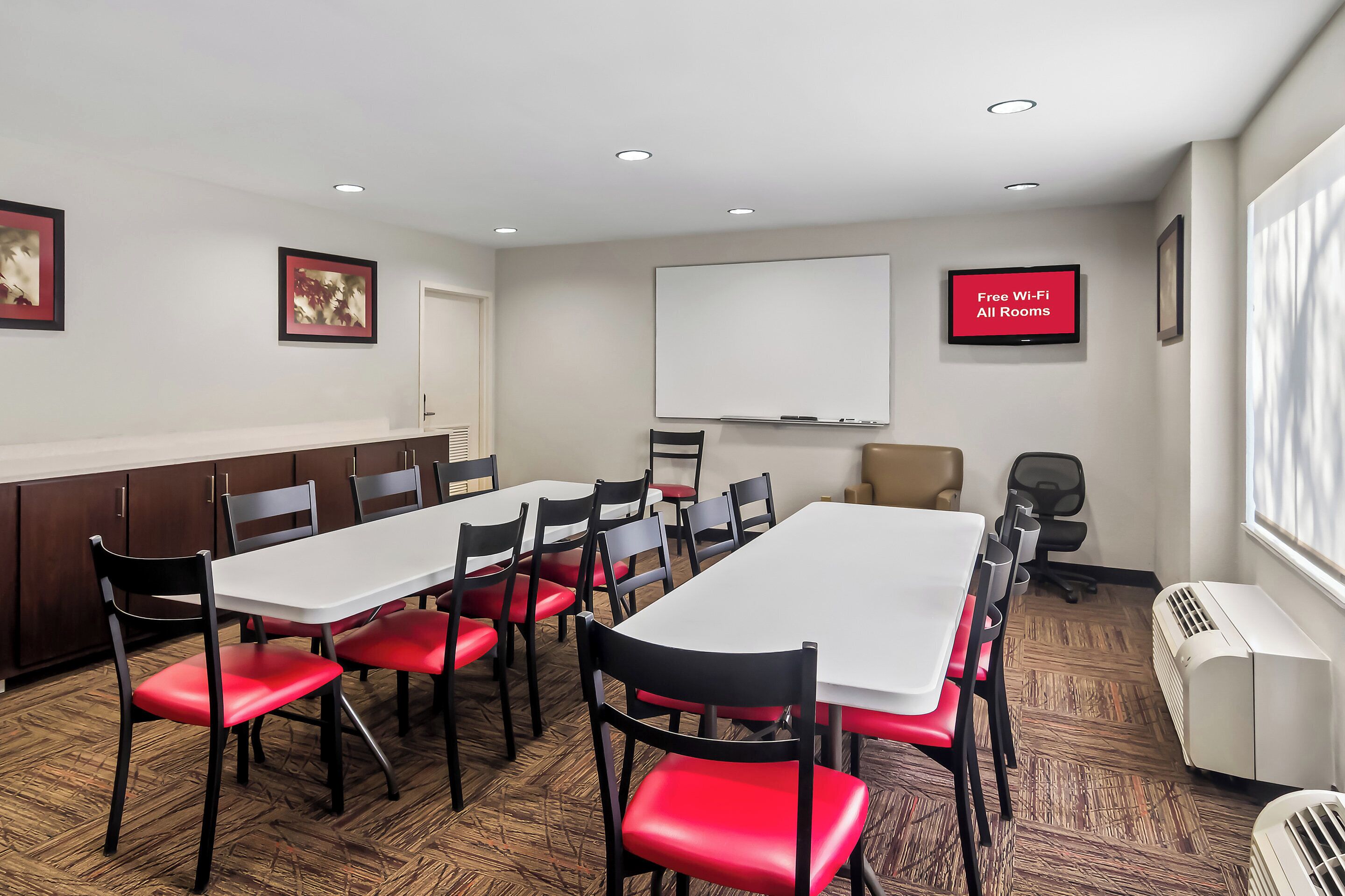 A conference room with a white table, red chairs, a whiteboard, and a TV screen advertising free Wi-Fi.