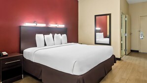 A hotel room with a large bed, a nightstand, a mirror, and a door.