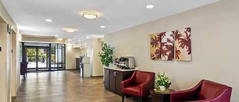 A reception area with a reception desk, two red chairs, a potted plant, and artwork on the wall.