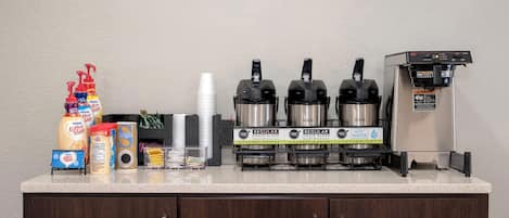 A coffee station with a coffee machine, sugar, creamer, and a coffee cup.