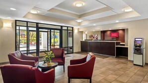 Un hall d’hôtel avec des fauteuils rouges, un comptoir d’accueil et un kiosque numérique.