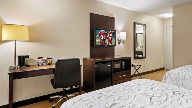 Hotelkamer met een bed, een bureau met een computer, een stoel, een televisie, een magnetron en een koelkast.