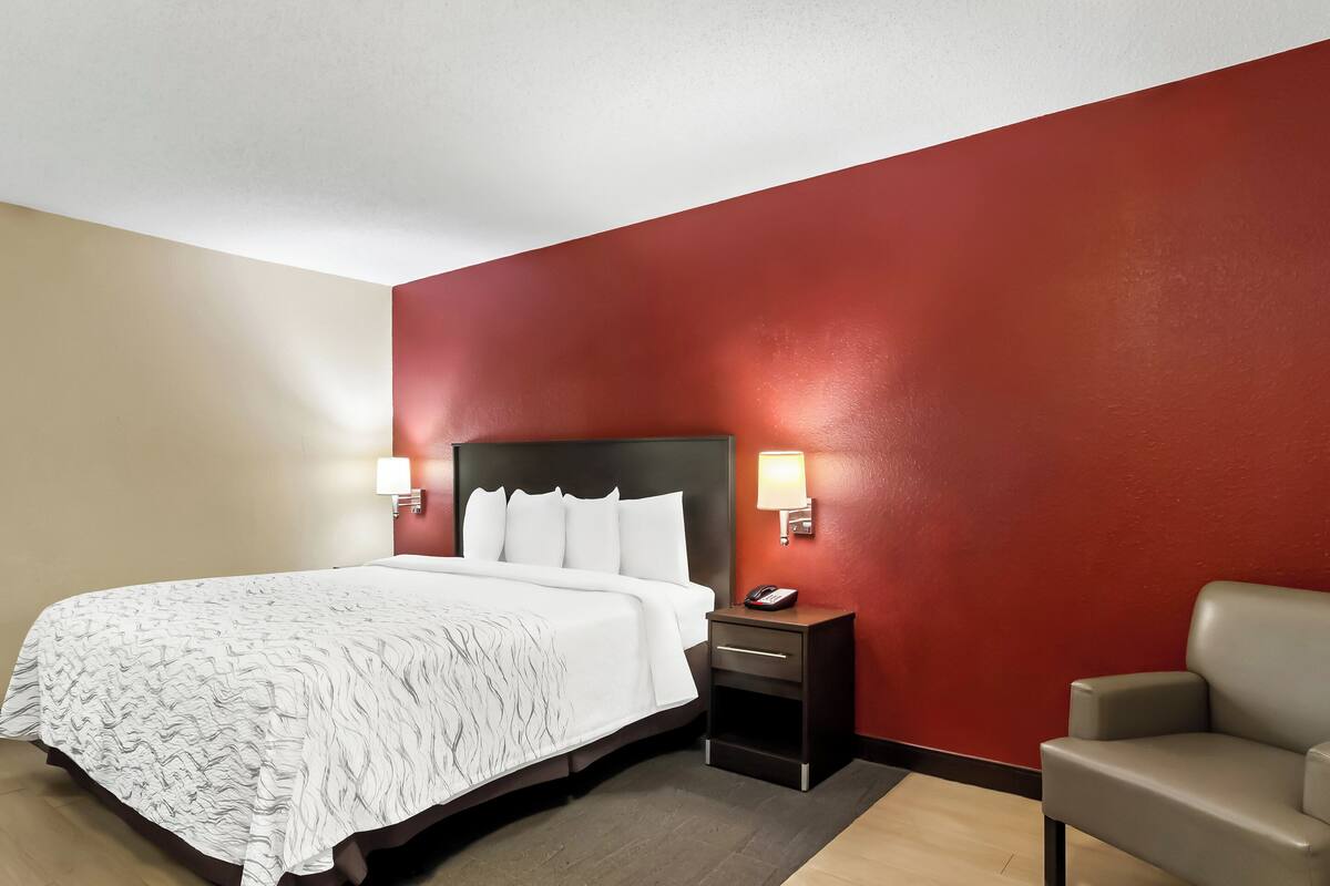 Ein Hotelzimmer mit Bett, Nachttischen, einem Sessel und roten Wänden.