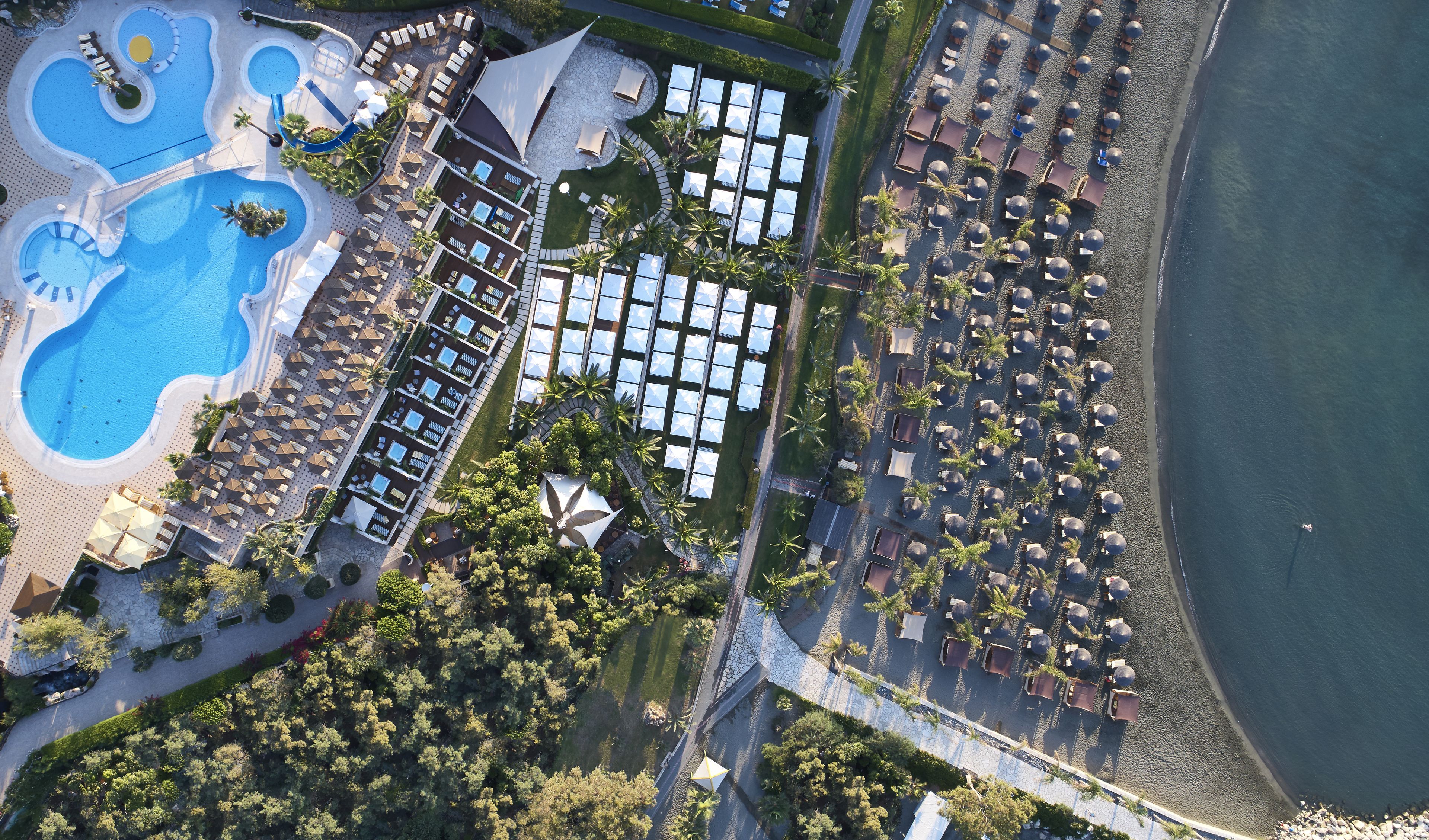 An aerial view of a resort with a large pool, multiple lounge areas, and a beachside section.