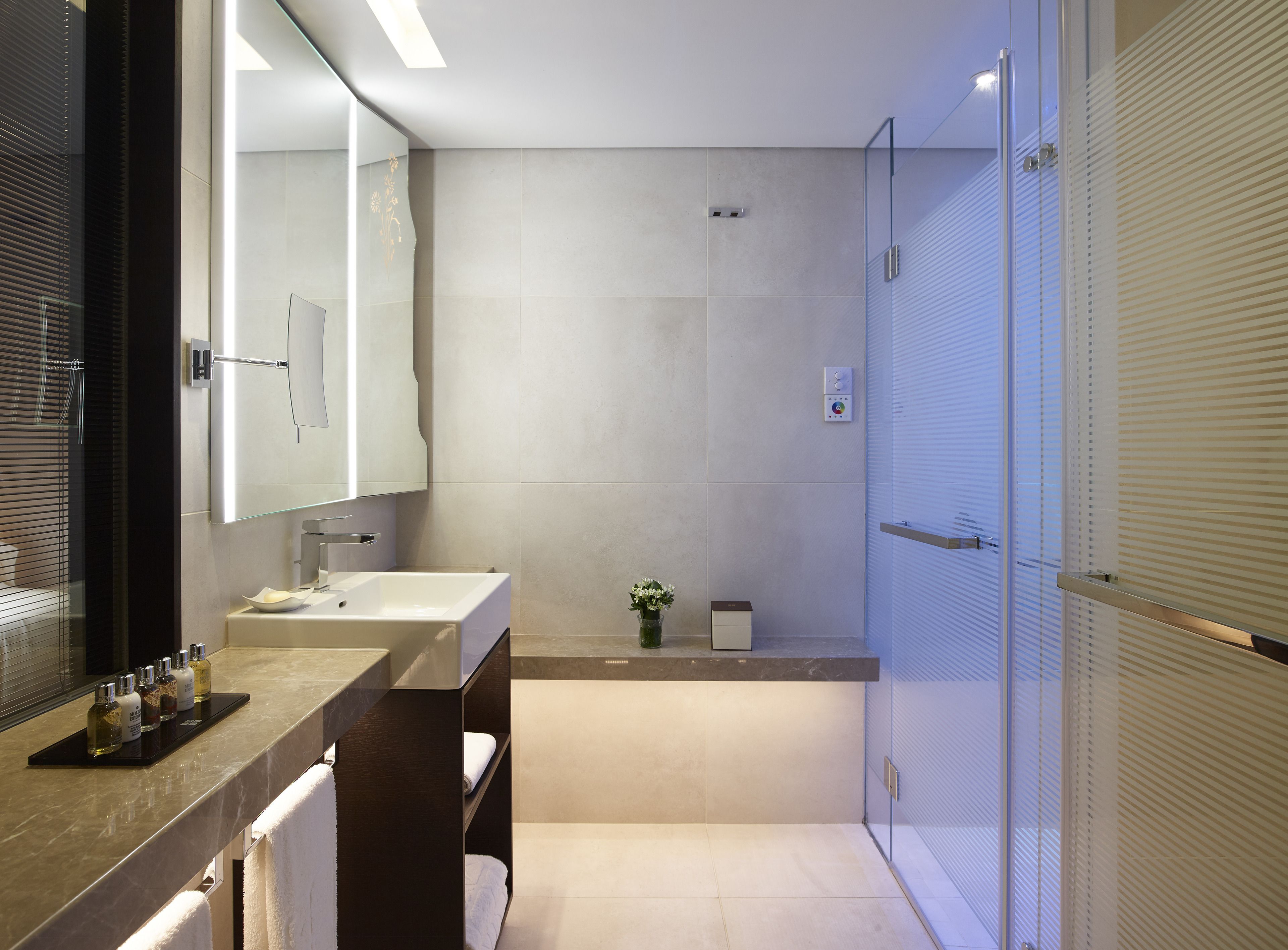 A modern bathroom with a large mirror, two sinks, a shower, and a towel rack.
