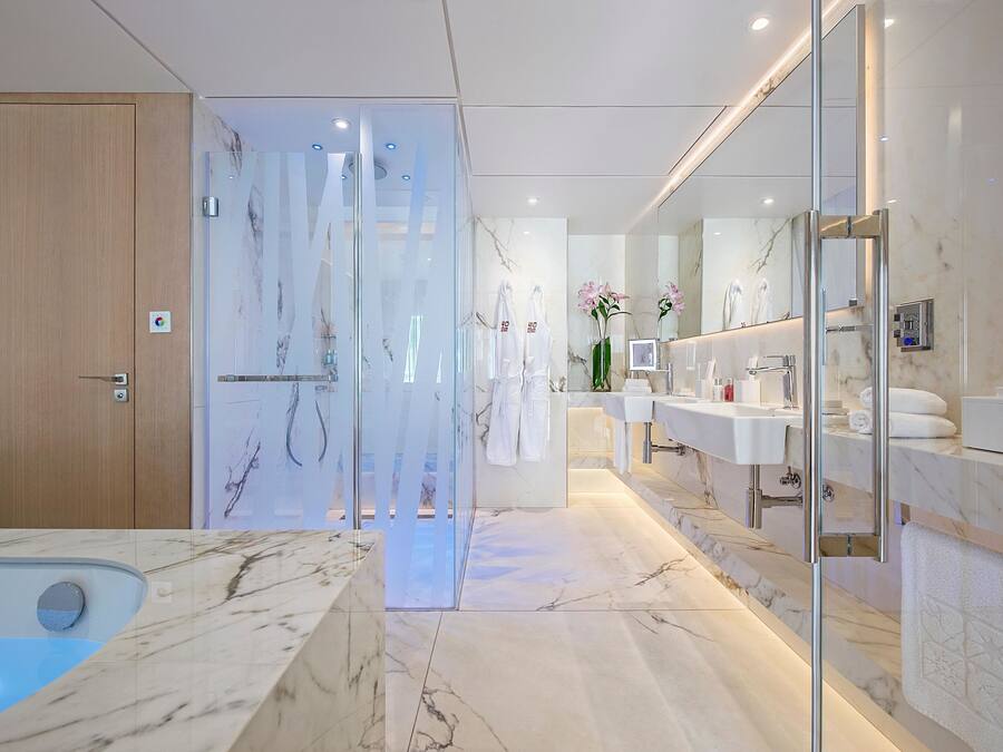 A modern bathroom with a marble floor, a glass shower enclosure, and a large mirror.